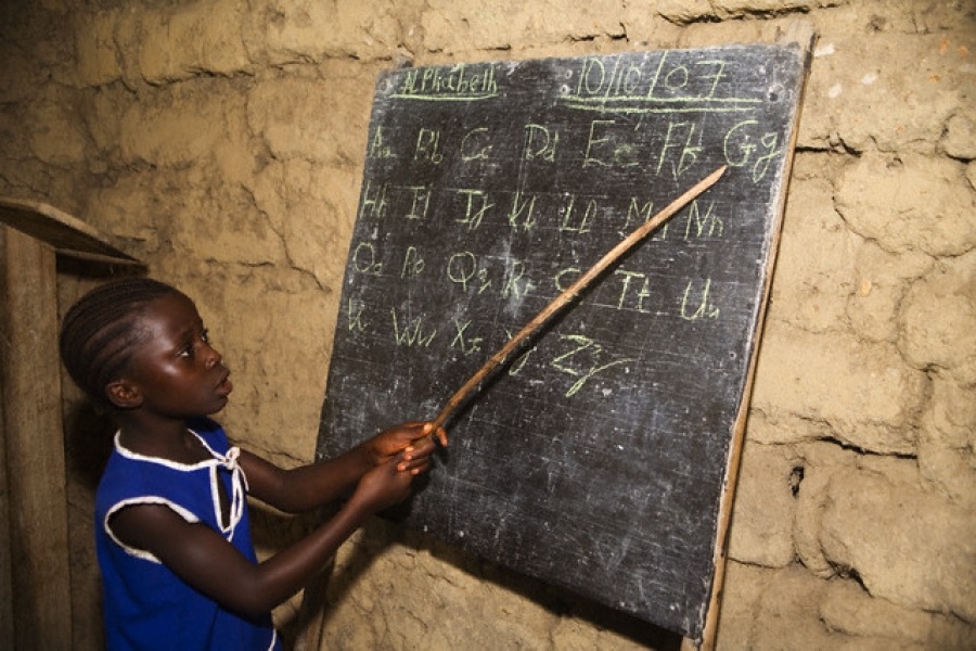 A child writing the alphabet on a blackboard at a community learning session in Northern Uganda
